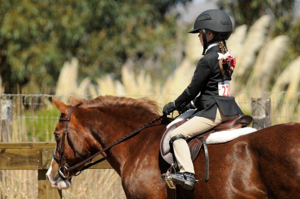 Young rider wearing paddock boots riding a pony at a show.