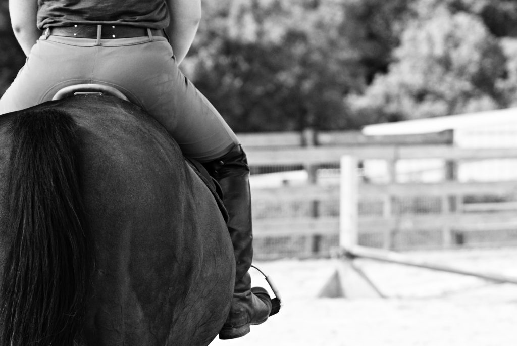 Black and white image of rider wearing breeches while riding a horse.