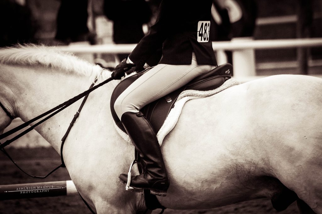 Black and white image of an English rider dressed in show attire riding a horse.