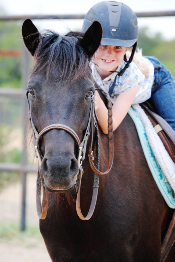 Smiling young rider on dark brown pony at summer riding camp.