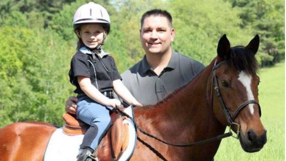 Dad standing next to young daughter on bay pony for Father's Day ride.