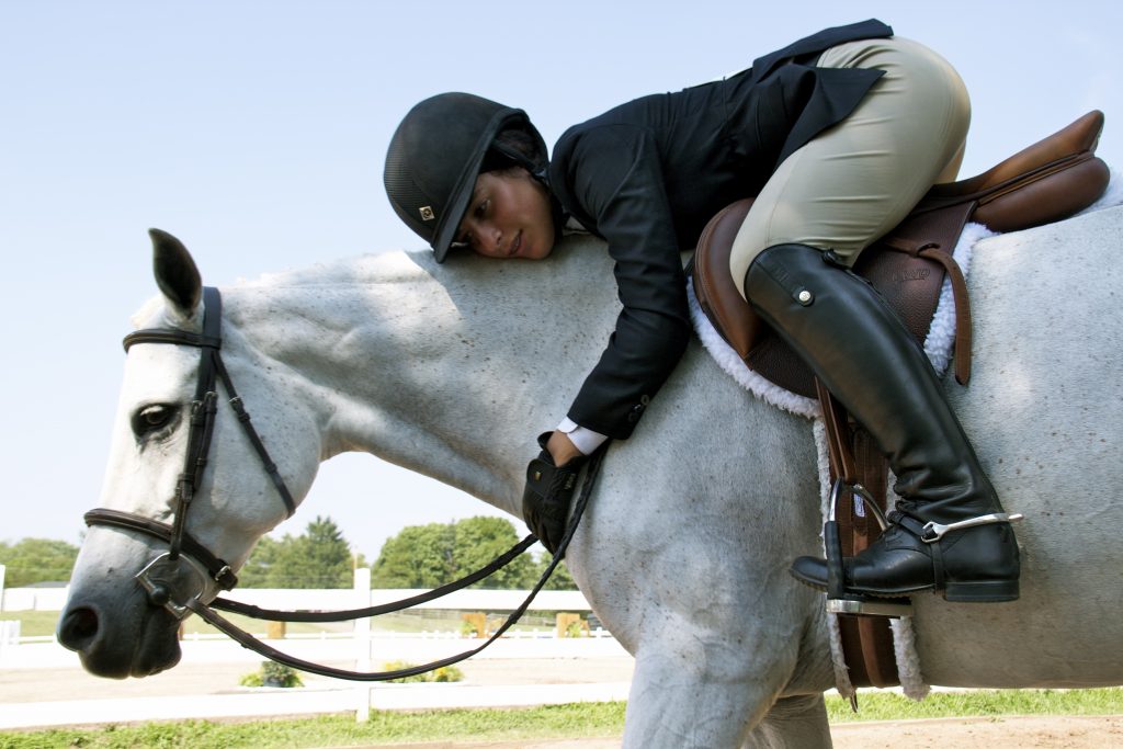 English rider in the saddle leaning down to hug her grey horse's neck.