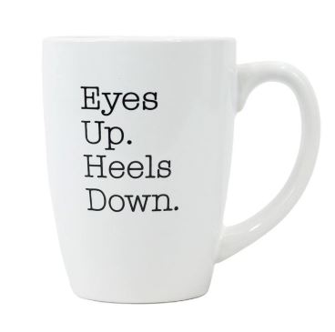 White coffee mug with text reading "Eyes Up. Heels Down."
