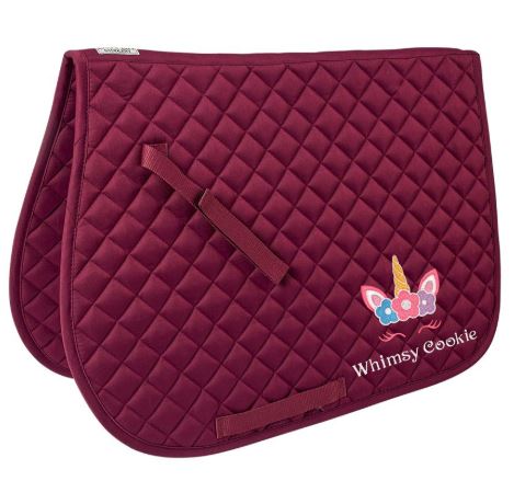 Burgundy colored quilted saddle pad with colorful unicorn monogram in lower right corner above the monogrammed name, "Whimsy Cookie."