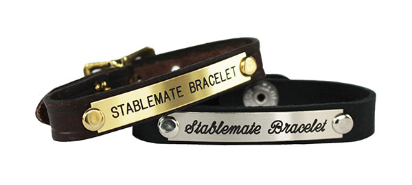 Two leather bracelets, one with a brass plate and one with a German silver plate are shown against a white background. Both bracelets are engraved with the words "Stablemate Bracelet". 