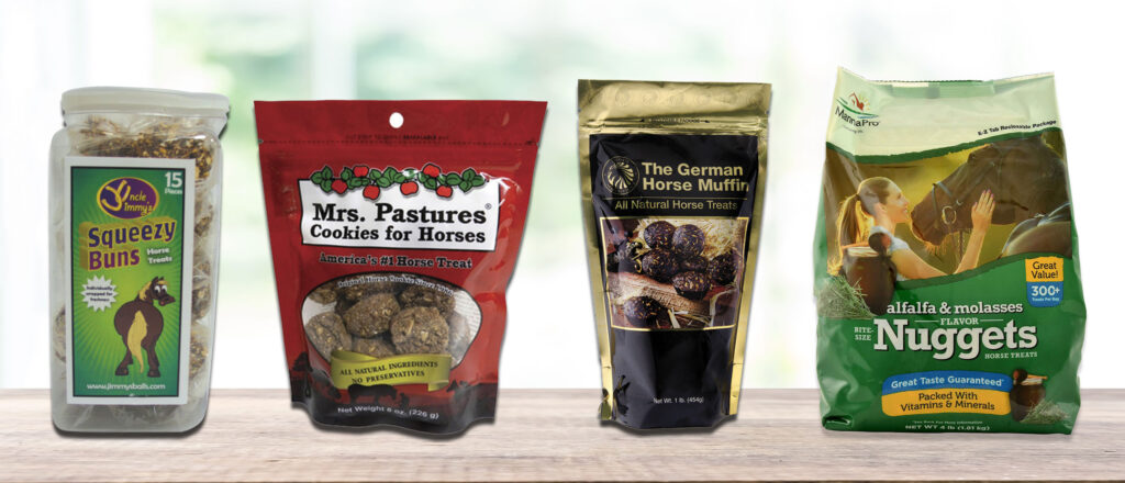 Four containers of horse treats are lined up on a wooden surface. From left to right the horse treat brands are Uncle Jimmy's Squeezy Buns, Mrs. Pastures Cookies for Horses, The German Horse Muffin, and Manna Pro Nuggets.