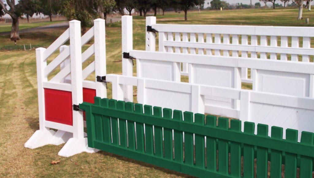 A set of four jumps stacked in ascending order. The front jump has a green gate with white and red jump standards. The jumps behind it are completely white.