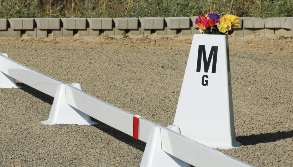 A white dressage letter cone the the letters M and G on it with colorful artificial flowers coming out of the top. 